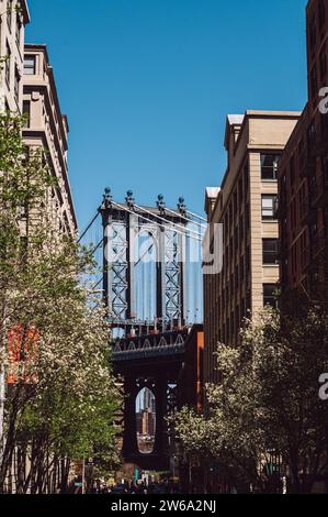 Una vivace scena di strada a DUMBO, Brooklyn, che cattura l'iconico ponte di Manhattan incorniciato tra due edifici storici in mattoni. Foto Stock