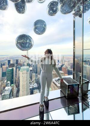 Una giovane e felice viaggiatrice che interagisce con palloncini d'argento sulla piattaforma di osservazione Summit One Vanderbilt nella sala Affinity di New York aga Foto Stock