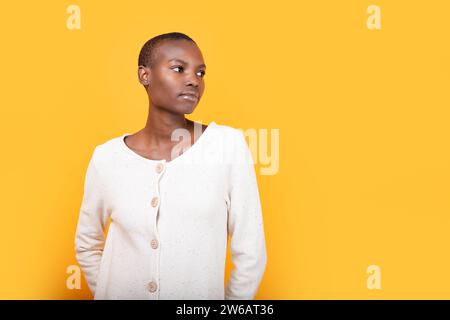 Ritratto di una giovane donna afro-americana sicura di sé e calma con i capelli corti in bianco, mentre si guarda lontano sullo sfondo giallo Foto Stock