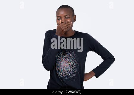 Felice giovane modello di moda afroamericano che copre la bocca con la mano su sfondo bianco Foto Stock