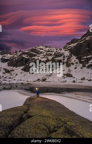 Un avventuriero solitario si erge tenendo una luce su un affioramento di muschi islandesi, con spettacolari cieli al crepuscolo dipinti con sfumature di rosa e viola sopra rugge Foto Stock