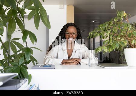 Ritratto di una giovane donna d'affari afroamericana che sorride mentre si siede alla scrivania in ufficio Foto Stock
