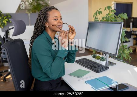 Giovane donna d'affari afroamericana che indossa occhiali da vista mentre è seduta alla scrivania del computer in ufficio Foto Stock