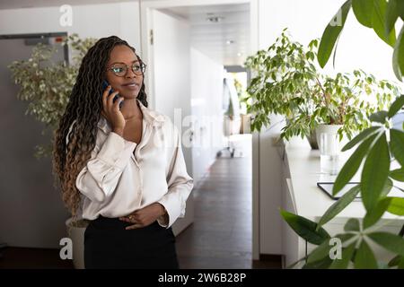 Giovane donna d'affari afroamericana premurosa che usa lo smartphone mentre si trova in ufficio Foto Stock