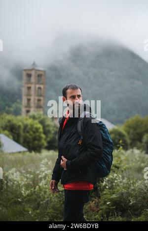 Un premuroso uomo con zaino in spalla in abiti caldi mentre si cammina contro una montagna sfocata e lussureggiante nel parco nazionale della Catalogna Foto Stock