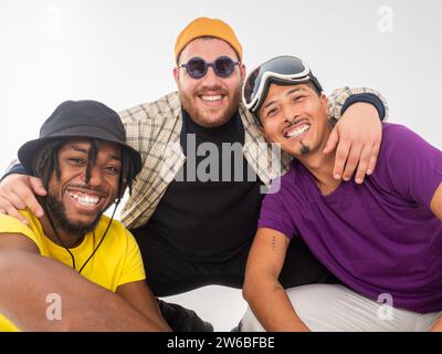 Tre uomini allegri che indossano abiti casual ed eleganti sorridono e si abbracciano per mostrare il loro cameratismo su uno sfondo bianco Foto Stock