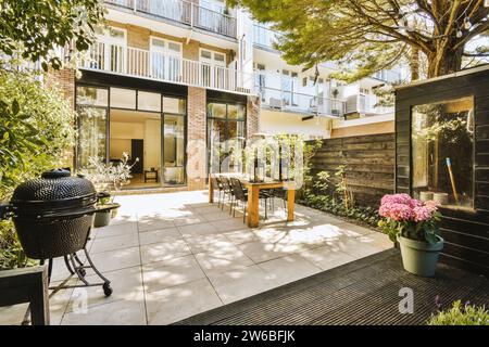 Tavolo con sedie e barbeque nel patio all'esterno della casa moderna con piante e recinzione nel cortile privato sul retro Foto Stock