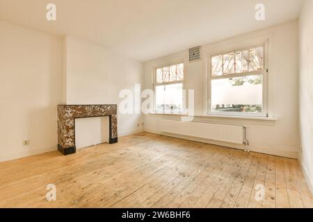 Caminetto e radiatore nel soggiorno non arredato di una casa contemporanea con pavimento in legno duro e finestre luminose Foto Stock