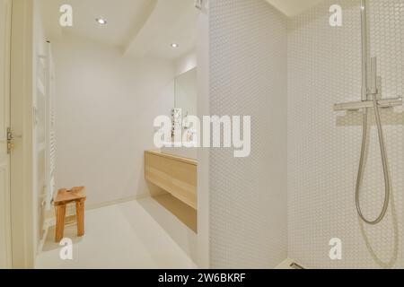 Bagno luminoso e moderno con lavandino in legno, grande specchio e spaziosa area doccia con piastrelle bianche. Foto Stock