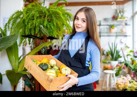 Giovane fioraio con capelli scuri che trasportano piccole zucche piene di cassa di legno mentre lavora in un fioraio Foto Stock
