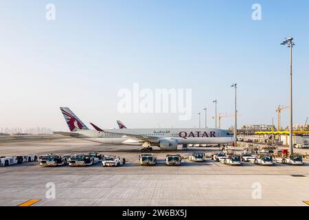 Vista laterale di un aereo Airbus A350-900 della Qatar Airways e di un aereo Douglas che trainano trattori in piedi nell'aeroporto internazionale Hamad di Doha, Qatar Foto Stock