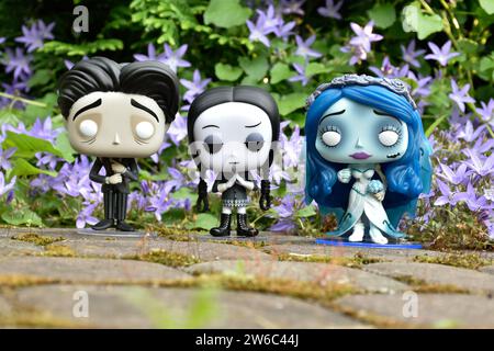 Funko Pop action figure di Victor ed Emily del film d'animazione dark fantasy in stile gotico Corpse Bride e Wednesday Addams. Fiori blu, muschio, strada di pietra. Foto Stock