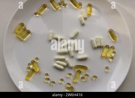 un grande piatto bianco con una dispersione di capsule bianche e dorate con vitamine, un integratore alimentare biologico sotto forma di complesso di vitamine Foto Stock