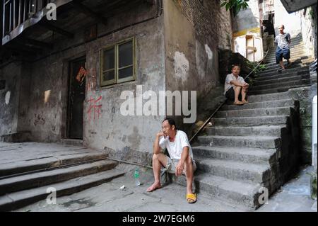 04.08.2012, Cina, Chongqing, - gli uomini si siedono sui gradini di fronte ad un vecchio edificio residenziale nella città vecchia di Shibati, nel distretto di Yuzhong di Th Foto Stock