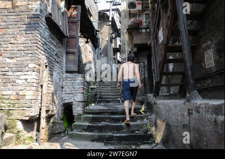 04.08.2012, Cina, Chongqing, - Un uomo che sale una vecchia scalinata in pietra nell'area delle diciotto scale, superando le case tradizionali nella città vecchia dello Shi Foto Stock