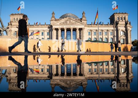 21.10.2023, Germania, Berlino, - la gente cammina davanti al Reichstag nel quartiere Mitte di Berlino in una soleggiata giornata autunnale, la sua faÁade occidentale si riflette in una grande Foto Stock