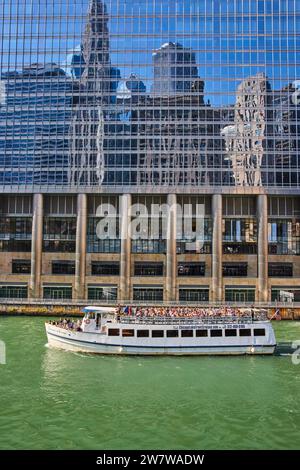 Crociera turistica in barca sul canale di Chicago con edificio riflettente che mostra cielo blu e grattacieli Foto Stock