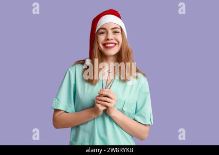 Ritratto di una giovane dentista femminile nel cappello di Babbo Natale con attrezzi su sfondo viola Foto Stock
