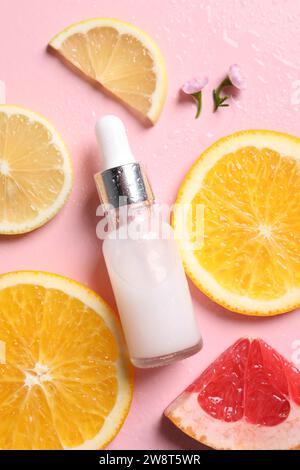 Bottiglia di siero cosmetico, agrumi a fette e fiori piccoli su sfondo rosa bagnato, piatto Foto Stock