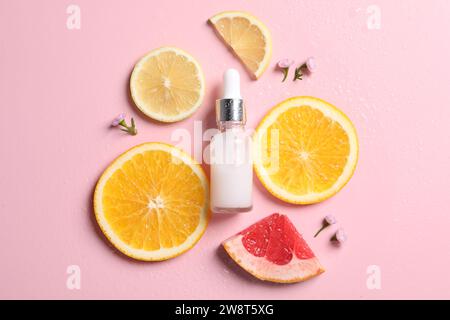 Bottiglia di siero cosmetico, agrumi a fette e fiori piccoli su sfondo rosa bagnato, piatto Foto Stock
