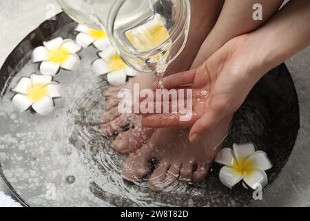 Donna che versa acqua sulla mano mentre immerge i piedi nella ciotola sul pavimento, sopra la vista. Trattamento spa Foto Stock