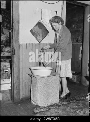 Giovane moglie di un minatore che aspira acqua al rubinetto nella sua cucina. Questo rubinetto è stato installato da un ex inquilino, poche case... Foto Stock
