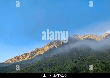 Vista delle Alpi al tramonto in una soleggiata serata d'estate. Il cielo è blu, con le vette delle montagne che catturano gli ultimi raggi del sole a metà strada. Foto Stock