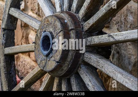 Primo piano del vecchio asse della grande ruota di legno di un antico carrello. L'assale è realizzato in ferro e legno e le razze in legno si estendono da Foto Stock