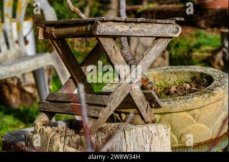 Primo scatto di un piccolo tavolo da giardino pieghevole, asciutto, vecchio, tra gli altri utensili, utensili e vasi da giardinaggio, in vista dell'attesa autunnale, vecchia, fredda e decadente Foto Stock