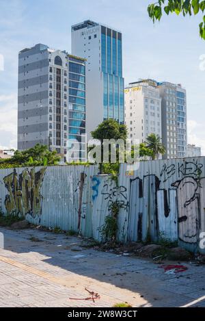 Da Nang, Vietnam - 4 ottobre 2023: Una recinzione in costruzione e un marciapiede sporco con alti hotel sul mare sullo sfondo. Foto Stock