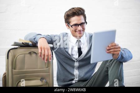 Uomo d'affari, lettura o valigia con tablet, pavimento e sorriso con app, volo o viaggio sullo sfondo della parete. Imprenditore, persona o touchscreen acceso Foto Stock