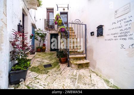 Scena di strada con un piccolo cortile tra case, balconi, scalinata e piante verdi in vaso. Foto Stock