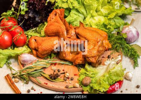 Ali di pollo affumicate con erbe fresche, pomodori e altri condimenti su un tagliere Foto Stock