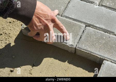 Un lavoratore poggia lastre di pavimentazione sulla sabbia in un cantiere edile Foto Stock