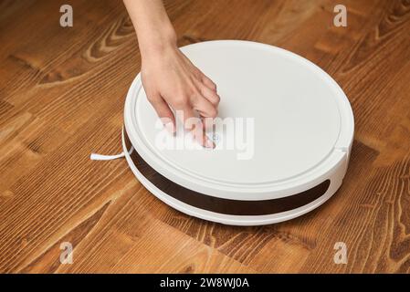 Una donna accende un aspirapolvere robot per pulirlo Foto Stock