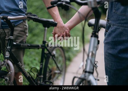 Coppia a un appuntamento che si tiene per mano mentre cammina in bicicletta Foto Stock