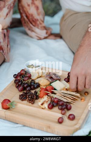 Le mani afferrano la frutta dal tagliere di salumi durante la serata del giorno Foto Stock