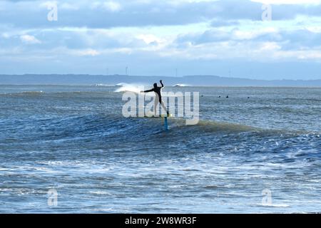 Il surfista in lamina con le mani tenute in alto vola sulla superficie dell'onda. Foto Stock