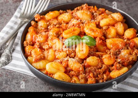 Gnocchi di patate caldi con salsa bolognese tradizionale e primo piano di parmigiano sul piatto sul tavolo. Orizzontale Foto Stock