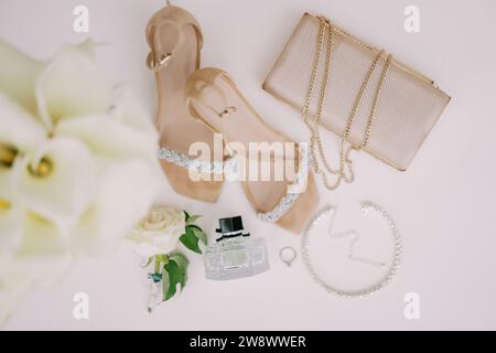 La fede nuziale si trova su un tavolo bianco vicino alle scarpe da sposa, alla borsa e al profumo. Vista dall'alto Foto Stock