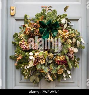 Corona di Natale fatta di rami di abete, con coni di pino, ortensie, rami di eucalipto, arance essiccate e arco verde su una porta grigia di Londra. fil. Quadra Foto Stock