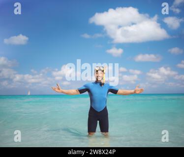 Giovane uomo felice che indossa un costume da immersione e una maschera e si trova in acqua Foto Stock