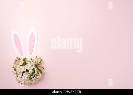 Buona Pasqua. Orecchie di coniglio in carta rosa e bouquet rotondo di fiori di ciliegio o mela freschi su sfondo rosa. Auto di benvenuto di Pasqua Foto Stock