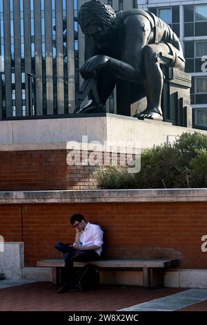 Uomo che legge un libro sotto la statua in bronzo di Sir Isaac Newton di Eduardo Paolozzi alla British Library , Londra, Inghilterra Foto Stock