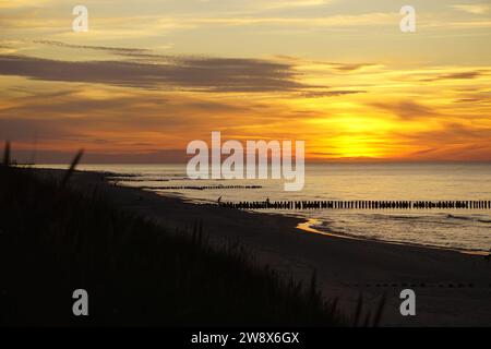 Un bellissimo tramonto sul Mar Baltico in Germania. Il cielo, di colore arancione, è leggermente nuvoloso e l'ampia spiaggia sabbiosa incontra il mare calmo. Mar Baltico, Germania Foto Stock