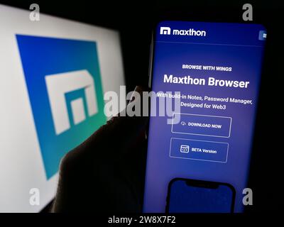 Persona che possiede il cellulare con la pagina Web dell'azienda di browser Web Maxthon davanti al logo aziendale. Concentrarsi sul centro del display del telefono. Foto Stock