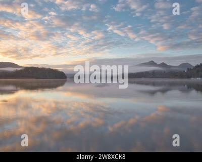 Dalle coste settentrionali di Derwentwater, una vista ininterrotta del sole che sorge sulla sua superficie calma e nebbiosa e sulle colline circostanti. Foto Stock