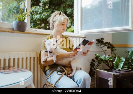 Donna con rivista di lettura di cani mentre era seduta nella sala d'attesa della clinica veterinaria Foto Stock