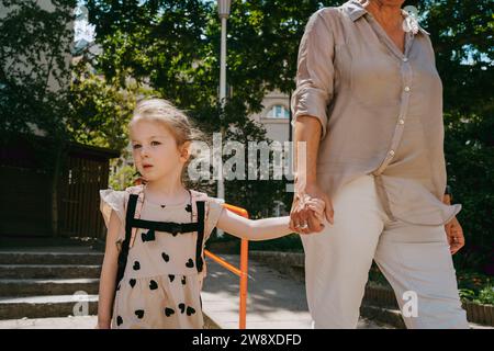 Donna anziana che si tiene per mano mentre cammina con la nipote all'asilo Foto Stock