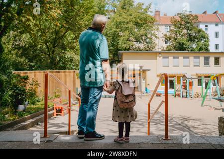 Uomo anziano con nipote in piedi vicino alla ringhiera all'asilo Foto Stock